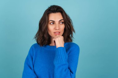 A woman in a blue knitted sweater and natural make-up, curly short hair, looks away thoughtfully, thinking about ideas clipart