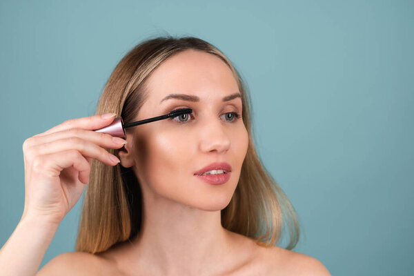 Закрытый портрет обнаженной женщины с идеальной кожей и естественным макияжем, обнаженными губами, держащей в руках маскару.