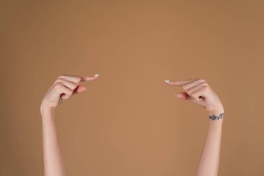 Bej bir arka planda kadın elleri, işaret parmakları boş alanın ortasına işaret ediyor