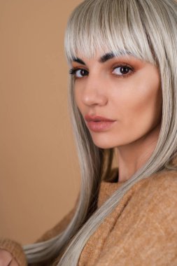 Kakülleri ve kahverengi gündüz makyajlı, bej arka planda seksi bir süveter giyen sarışın kız.