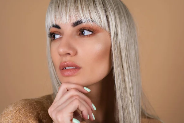 Blonde girl with bangs and brown daytime make-up in a sweater on beige background sensual fashion portrait