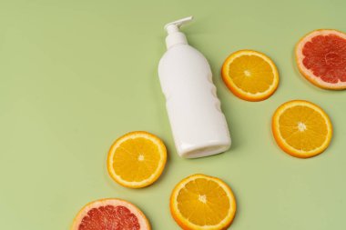 Doğal C vitamini, saç bakımı. Beyaz şampuan, losyon ve açık yeşil arka planda taze portakal ve greyfurt parçaları..