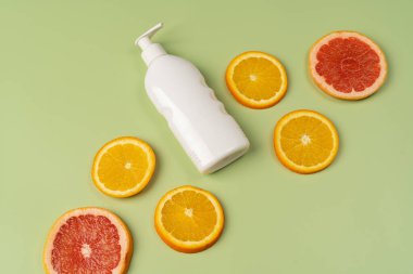 Doğal C vitamini, saç bakımı. Beyaz şampuan, losyon ve açık yeşil arka planda taze portakal ve greyfurt parçaları..