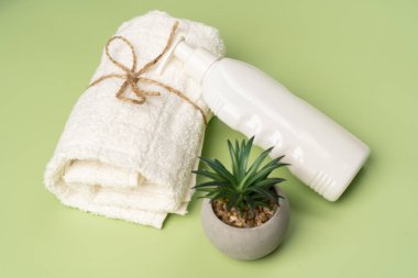 Beyaz bir şampuan ya da losyon şişesi, temiz temiz bir havlu ve açık yeşil arka planda kapalı bir süs bitkisi. Güzellik ve bakım saç ve vücut için..
