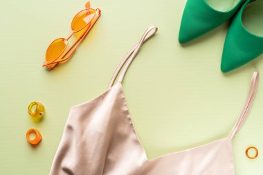Flatlay. Kadın kıyafetleri, turuncu gözlük, yüzük, ipek elbise ve açık yeşil arka planda topuklu ayakkabı..