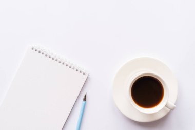 Üst kattaki ofis masasında yatıyordu. Not defterli çalışma alanı, ofis malzemeleri, beyaz arkaplanda kopya alanı olan kalem ve kahve fincanı.