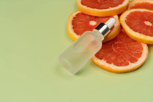 Natural vitamin C serum, skin care, essential oils. Cosmetic glass bottle with dropper and fresh juicy grapefruit slices.