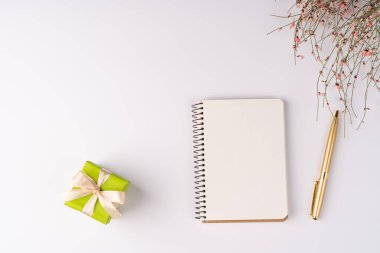Düz yatış, üst manzara, beyaz arka plan, küçük hediye kutuları ve 8 Mart için pembe sevimli çiçekli bir çalılık, bahar havası, not defteri ve kalem.