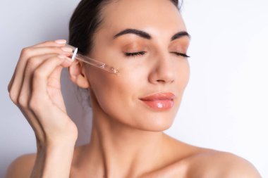 Mükemmel ciltli ve doğal makyajlı üstsüz kadının yakın güzellik portresi, gençlik ve cilt suyu için serum, kozmetik yağlı damlatıcı.