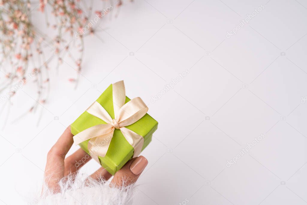 White background, cute dried flowers, a graceful female hand holds a small gift box, a gift for March 8, Women's Day