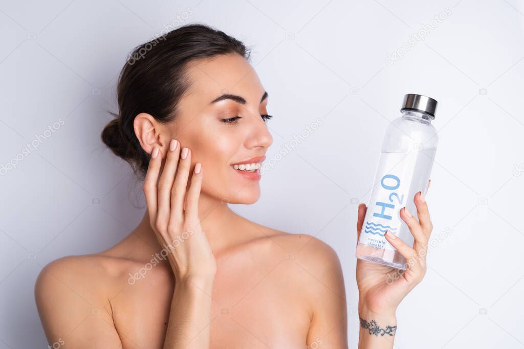 Close beauty portrait of a topless woman with perfect skin and natural make-up, holding personal glass bottle of h2o water, on a white background	