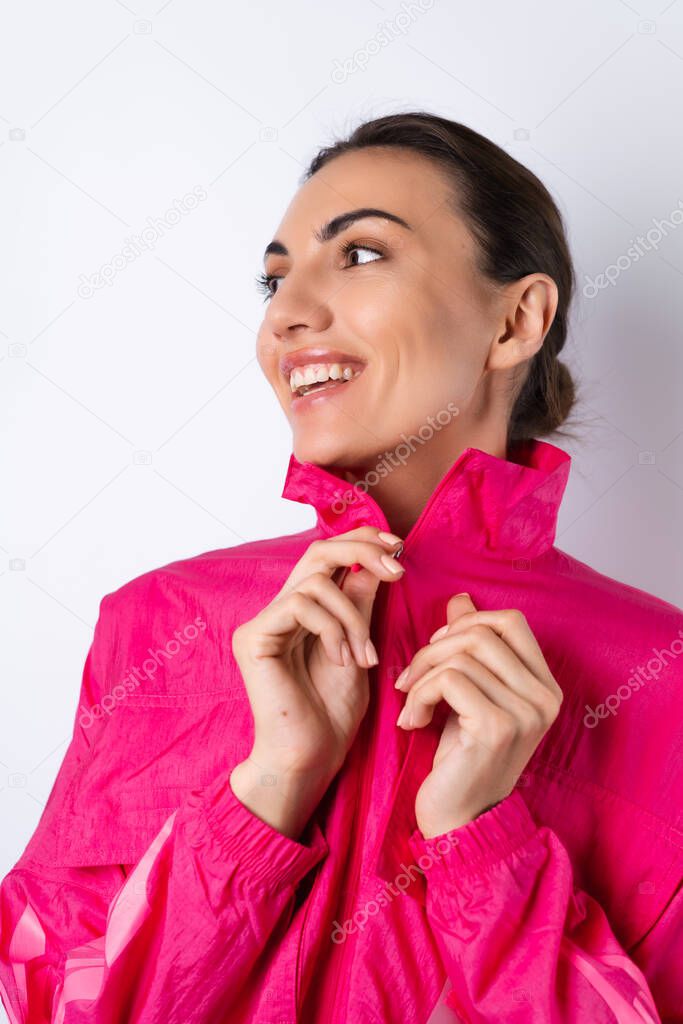A young woman in a bright pink sports jacket on a white background smiles cheerfully, vertical frame