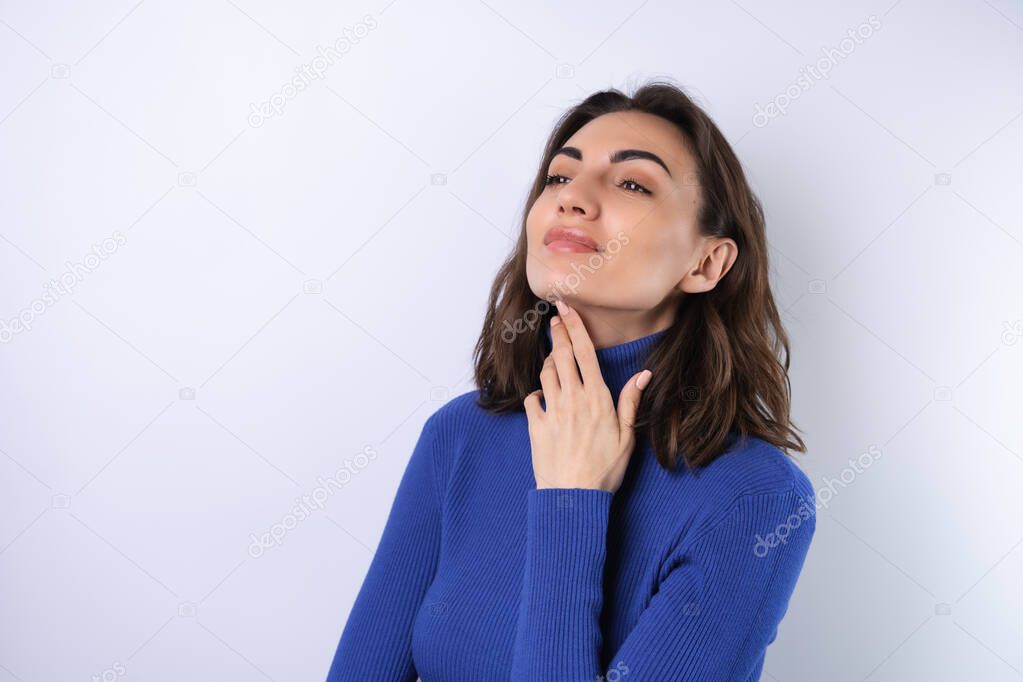 A young woman in a blue golf turtleneck on a white background with a confident smile looks to the side