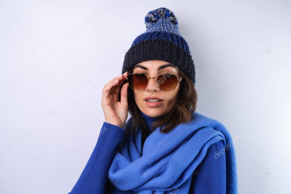 Young woman in a blue golf turtleneck, hat and scarf, sunglasses, on a white background