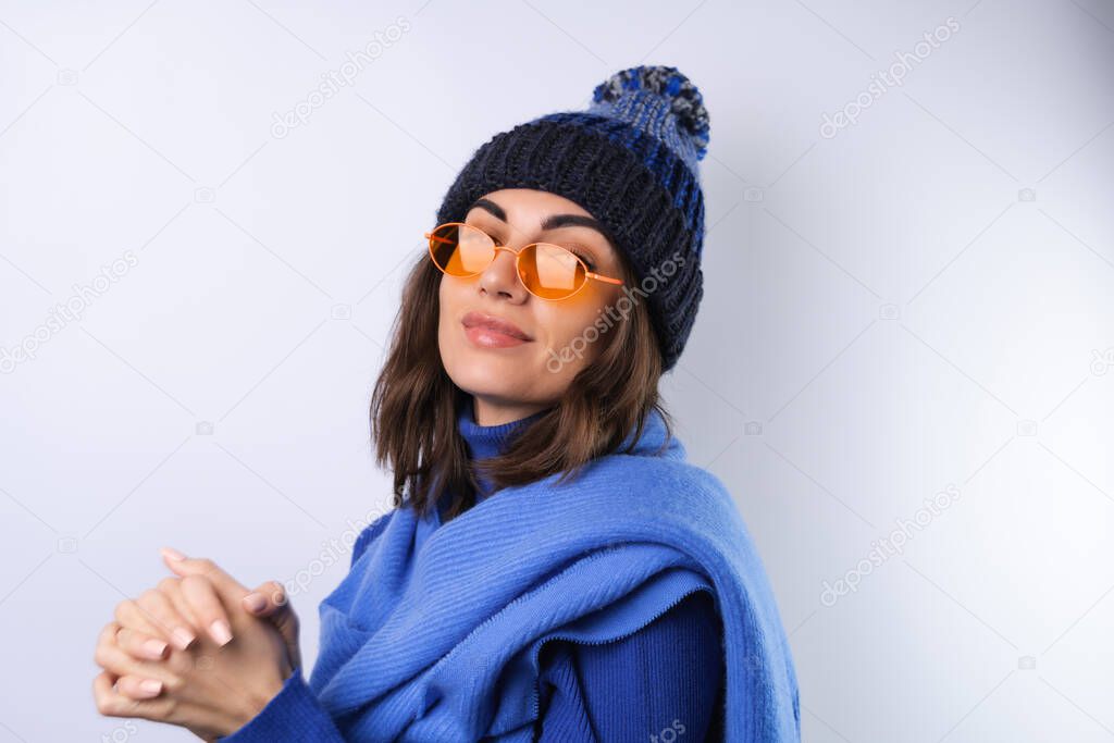 Young woman in a blue golf turtleneck, hat and scarf, sunglasses, on a white background, cheerful in a good mood