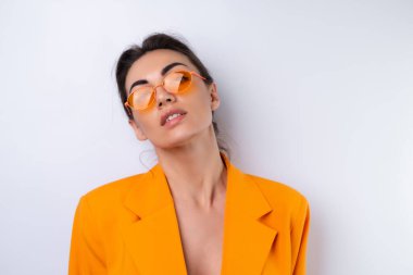 Moda gözlüklü genç bir kadın ve beyaz arka planda parlak turuncu büyük bir ceket.