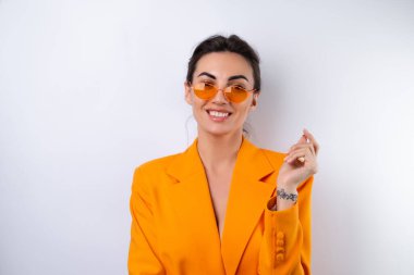 Moda gözlüklü genç bir kadın ve beyaz arka planda parlak turuncu büyük bir ceket.