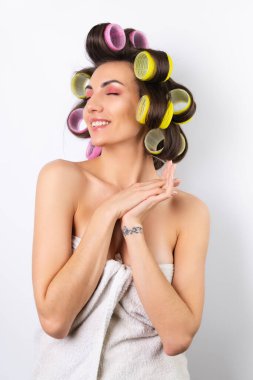 Güzel ev hanımı. Saç bigudileri ve çıplak omuzları olan neşeli genç bir kadın randevu gecesine hazırlanıyor. Beyaz bir arka planda evde saç stili yapar..