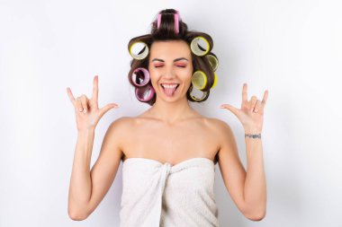 Güzel ev hanımı. Saç bigudileri ve çıplak omuzları olan neşeli genç bir kadın randevu gecesine hazırlanıyor. Beyaz bir arka planda evde saç stili yapar..