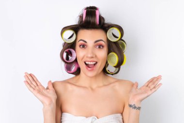 Güzel ev hanımı. Saç bigudileri ve çıplak omuzları olan neşeli genç bir kadın randevu gecesine hazırlanıyor. Beyaz bir arka planda evde saç stili yapar..