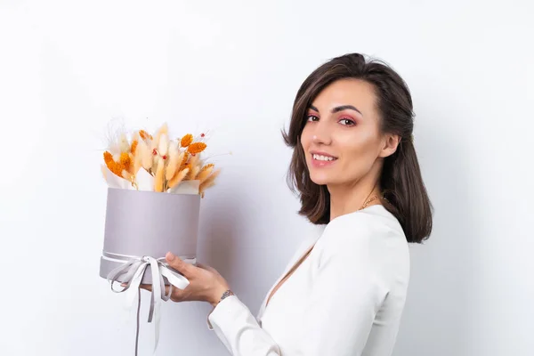 Young woman in a cocktail dress, gold chain, bright spring pink makeup on a white background. Holds a bouquet of orange dried flowers, a gift for March 8.