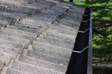 Koyu kahverengi metal yağmur oluğu olan ev çatısının ayrıntıları. Çatı, gri beton çatı kiremitleriyle kaplı. 