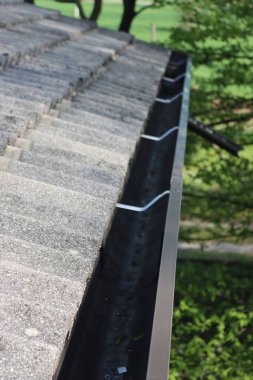 Koyu kahverengi metal yağmur oluğu olan ev çatısının ayrıntıları. Çatı, gri beton çatı kiremitleriyle kaplı. 