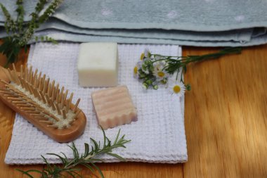 Sıfır atık kozmetik. Doğal organik katı el yapımı şampuan sabunlar ve nane, papatya çayı ve biberiye bitkisi havluların yanında ve ahşap masa üzerinde ahşap saç fırçası.