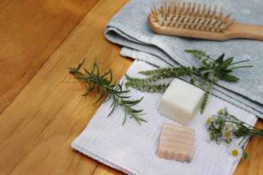 Sıfır atık kozmetik. Doğal organik katı el yapımı şampuan sabunlar ve nane, papatya çayı ve biberiye bitkisi havluların yanında ve ahşap masa üzerinde ahşap saç fırçası.