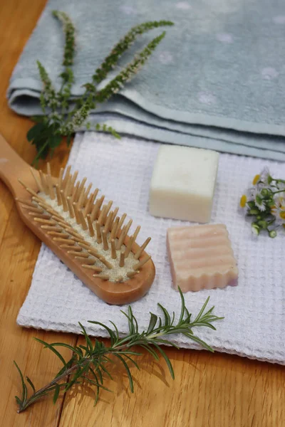 Sıfır atık kozmetik. Doğal organik katı el yapımı şampuan sabunlar ve nane, papatya çayı ve biberiye bitkisi havluların yanında ve ahşap masa üzerinde ahşap saç fırçası.