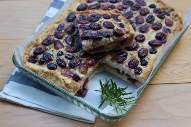 Sliced Italian Focaccia bread with sweet black grape and rosemary on a wooden table. Traditional dessert from Tuscany in Italy called schiacciata con l'uva