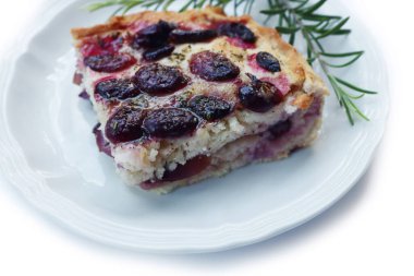 Slice of italian Focaccia bread with sweet black grape and rosemary on a plate on white. Traditional dessert from Tuscany in Italy called schiacciata con l'uva