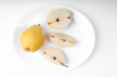 Sarı armutlar dilimlenmiş ve beyaz oval bir plaka üzerinde üst kısmı beyaz bir arka planda.