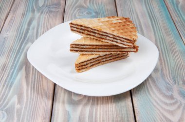 Beyaz bir tabakta, ahşap bir arka planda, birbirinin üstüne serilmiş üç lezzetli poğaça.