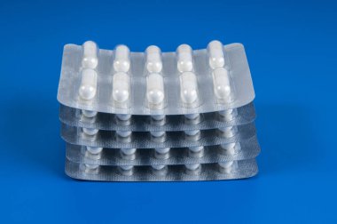 Mavi arka planda tedavi için beyaz haplarla dolu bir yığın plastik paket.