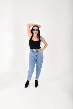 Stüdyoda, beyaz arka planda, güneş gözlüklü ve uzun pantolonlu şık bir kadın.