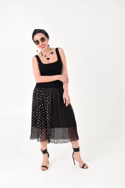 Siyah elbiseli güzel esmer bir kadının portresi. Stüdyoda beyaz bir arka planda gülümsüyor. Uzun güneş gözlükleriyle.