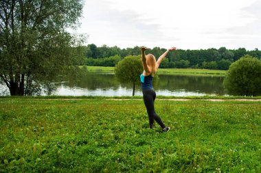 Parktaki sarışın ellerini sallayarak göletteki temiz havayı seviyor.
