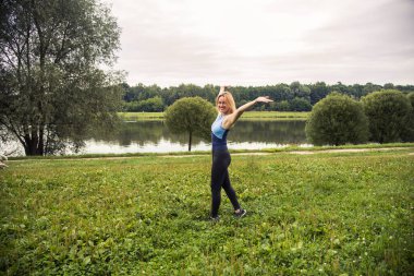 Parktaki sarışın ellerini sallayarak göletteki temiz havayı seviyor.