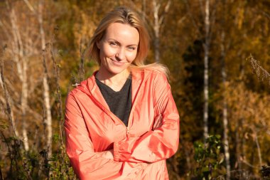 Güzel bir sarışın, bir orman parkında sarı sonbahar yapraklarının arka planında güzel bir gülümsemeyle yürüyor.