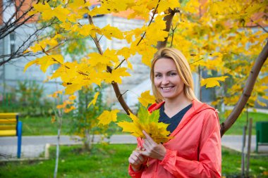 Güzel sarışın bir kızın portresi. Parkta açık havada gülüyor. Ağaçlardaki sarı sonbahar yapraklarının arka planında.
