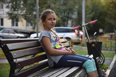 Bir yaz akşamı parkta açık havada bankta oturan küçük bir kızın portresi.