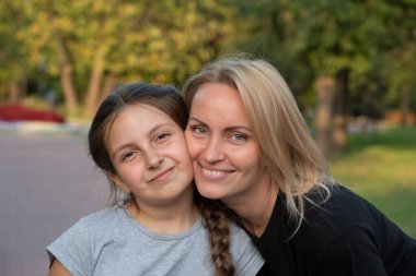 Anne ve kızı bir yaz günü parkta yanak yanağa sarılıyorlar.