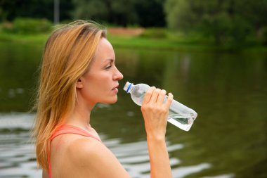 Parkta spor kıyafetleriyle sarışınlar. Nehir kenarında bir yaz günü su içiyorlar.