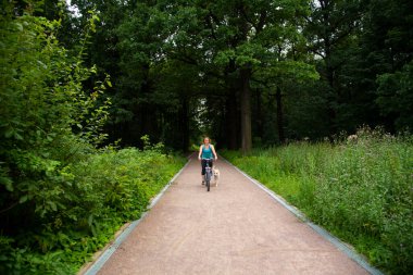 Parkta köpekle bisiklet süren güzel bir kız.