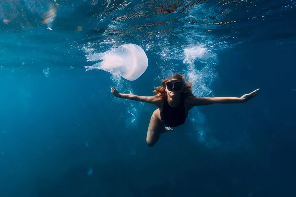Woman underwater with big jellyfish in blue ocean. Free diver underwater in transparent sea