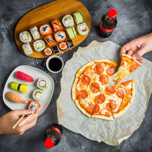 Food concept with pizza, sushi rolls, soda in bottle and hands take food. Flat lay
