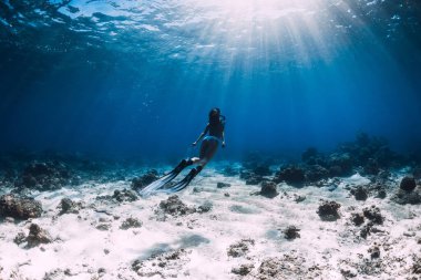 Bikinili özgür bir kadın tropik mavi okyanusta yüzgeçleri ile suyun altında süzülüyor.