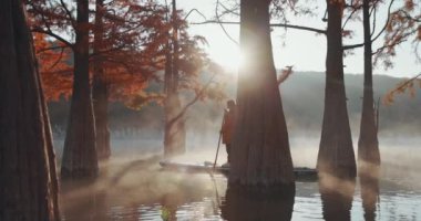 28 Ekim 2021. Anapa, Rusya. Güneş ışığı ve sonbahar taksonbahar ağaçlarıyla gölün üzerinde kürek çeken kadın.