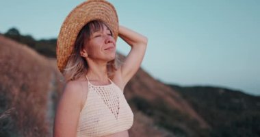 Şık bir genç kız kameraya günbatımı sıcacık bir ışıkla poz veriyor ve modaya uygun bir şapka takıyor. Mutlu bir kadının doğal güzelliği.